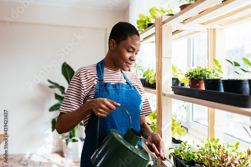 Black female irrigating plants on shelf