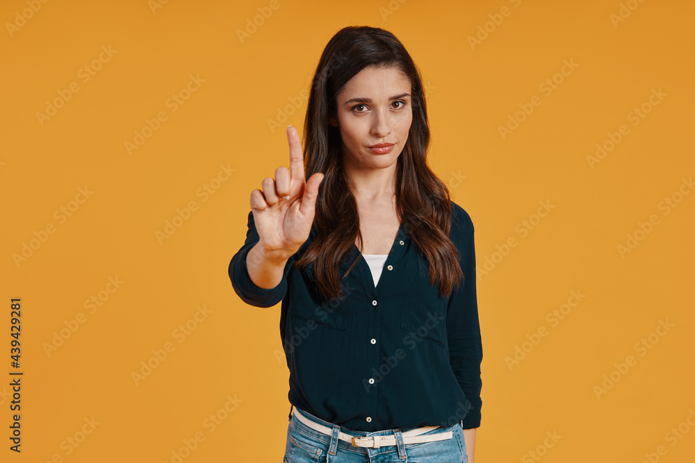 Attractive young woman in casual clothing gesturing while standing against yellow background Attractive young woman in casual clothing gesturing while standing against yellow background