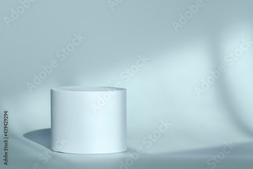 Blue round pedestal podium for packaging presentation on backdrop with room shadows from window. Circle platform stage for cosmetic products with geometric shadow on wall. Minimalist style