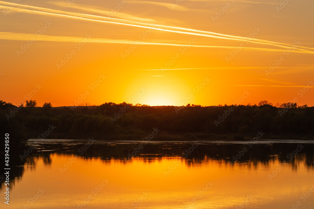 Smoke filled atmosphere causing a bright orange sunset with a reflection in a lake