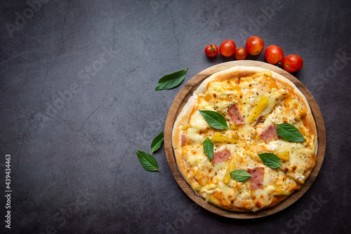 Tasty pizza homemade italian food style, pizza cheese ham and pineapple fruit cooking ingredients tomatoes basil on black background. Top view Flat lay