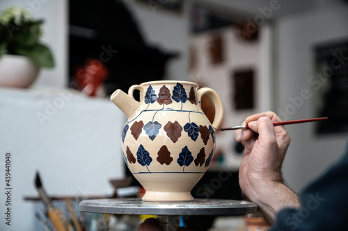 Person painting a ceramic vase with leaf shapes in a workshop. photo