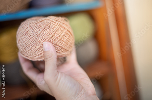 Female hand holding the beige yarn ball with the earth tone yarn in the wooden cupboard prepare for made Crochet and knitting.
