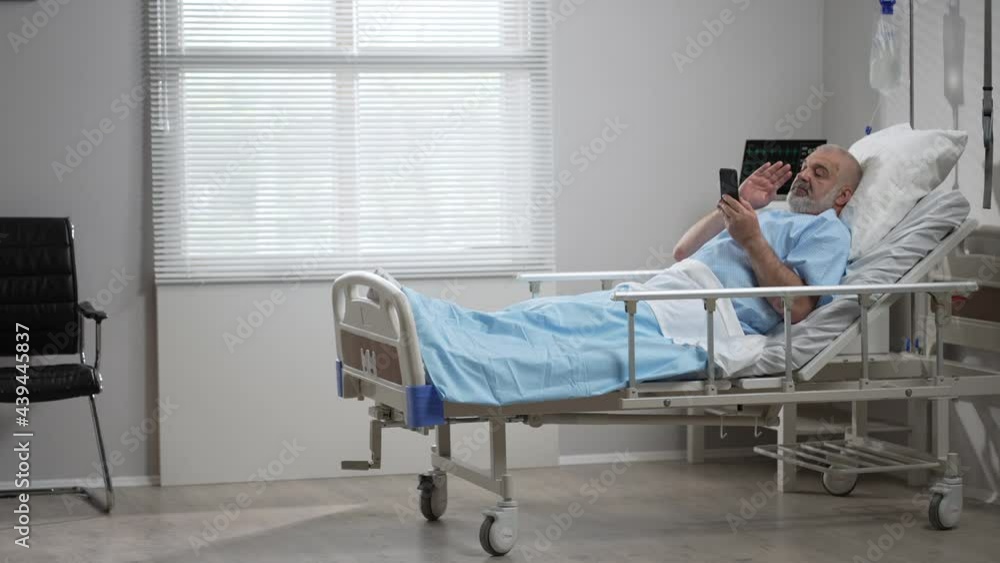 Hospital Ward: senior man Resting in Bed uses Smartphone for Video Call Conference Talk with Family and Friends. video call in hospital room Hospital Ward: senior man Resting in Bed uses Smartphone for Video Call Conference Talk with Family and Friends. video call in hospital room
