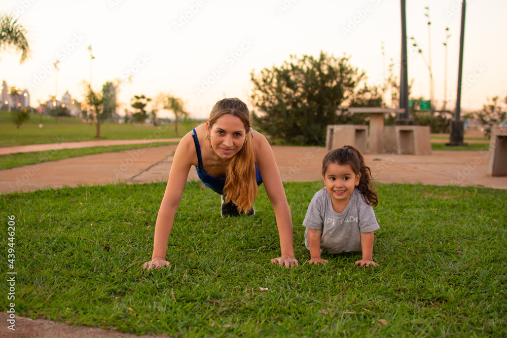 madre e hija haciendo flexiones de brazos en un parque al aire libre  - obrazy, fototapety, plakaty 