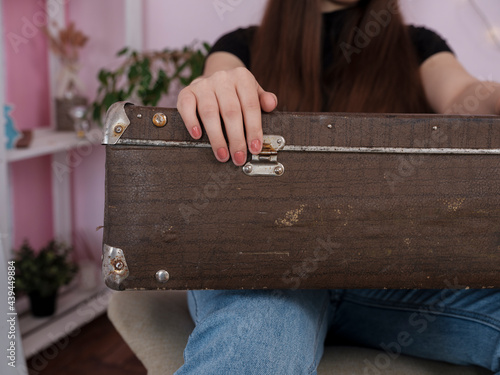 A woman is sitting with a suitcase indoors. Hand on a suitcase close up. Concept of going on vacation, travel.