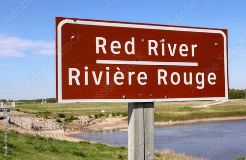 Close up of Red River road sign. White letters on a red background. The river is in the background