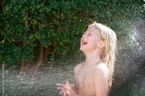 Young boy with long blonde hair laughs while getting sprayed with water photo