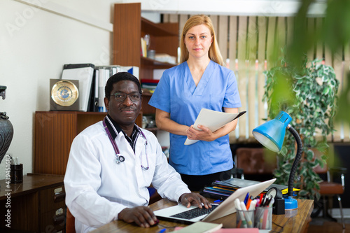 Portrait of two positive doctors of different nationalities, who are in the resident's office of the clinic with a ..folder of documents