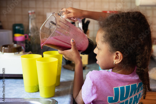 Young girl pouring blended smoothies into cups