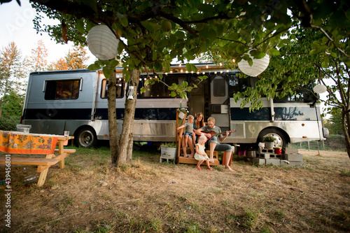 Young family sits on steps of RV playing guitar photo
