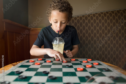 Boy playing checkers while sipping from cup
 photo