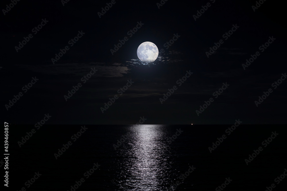 雲を帯びた満月が海に光の道を輝かせる