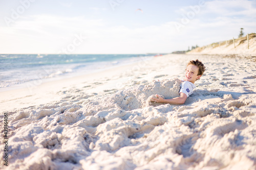 Smiling boy enjoying playing in sand at the beach on a sunny aft