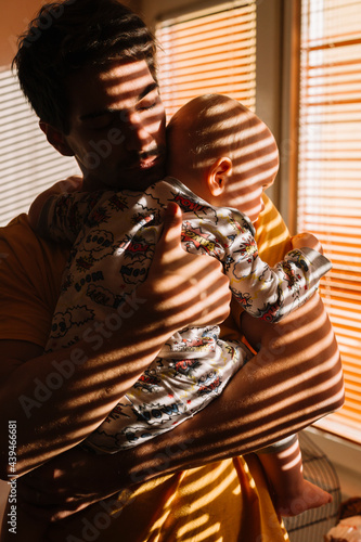 Father holds baby and lullaby by the darken window  photo