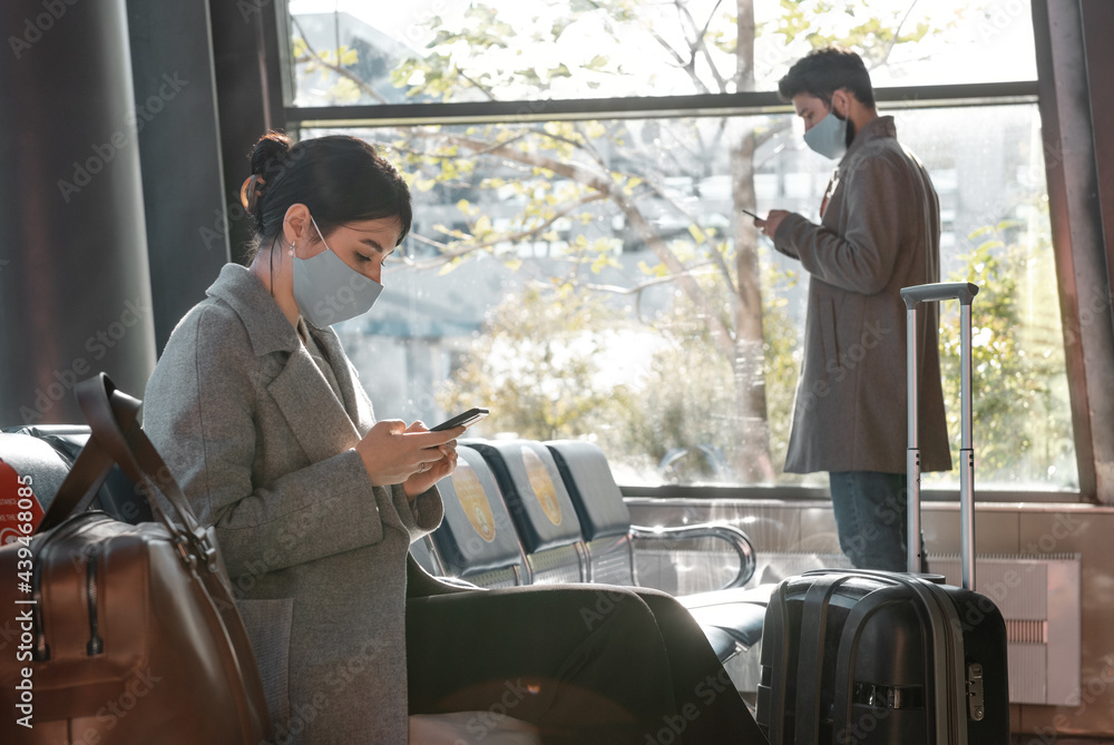 Travelers in masks browsing smartphones in airport waiting room Travelers in masks browsing smartphones in airport waiting room