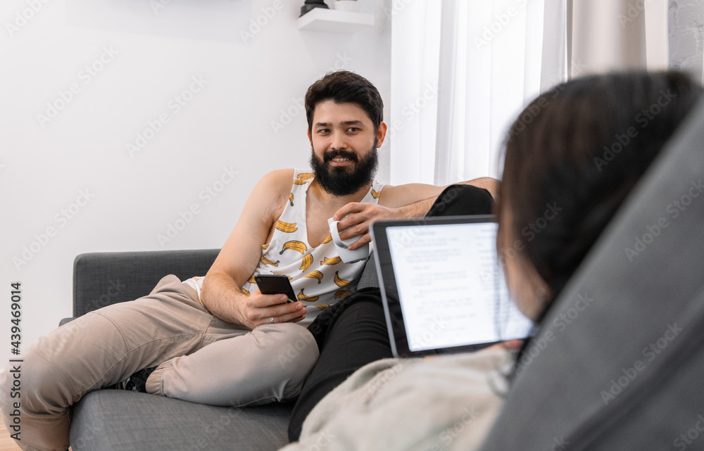 Man with smartphone and hot drink resting near woman with tablet Man with smartphone and hot drink resting near woman with tablet