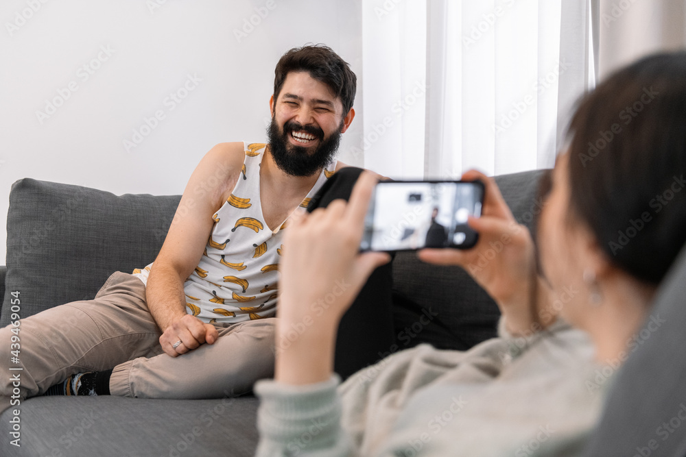 Woman taking photo of laughing man on couch Woman taking photo of laughing man on couch