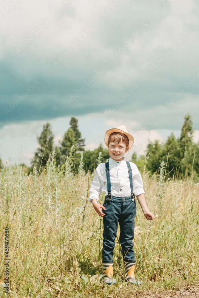 Little farmer on a summer field, cute little boy in a straw hat. boy with a flower stands in a field.
