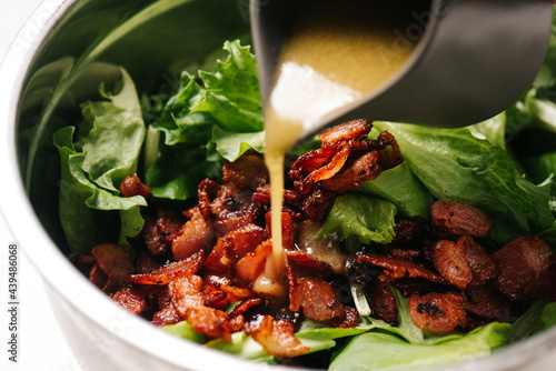 Pouring vinaigrette over bacon salad