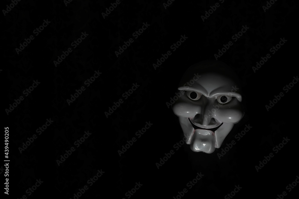 White scary mask on a black background with whites hand.