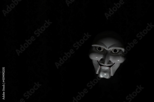 White scary mask on a black background with whites hand.
