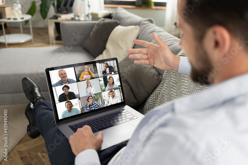 Young caucasian man using laptop for having virtual team meeting on video call with different people, work from home office or coworking, online meeting, briefing, brainstorming