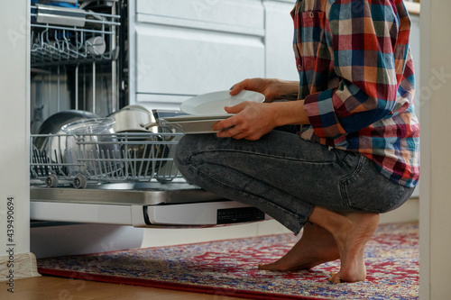 Crop woman sitting near open dishwasher photo