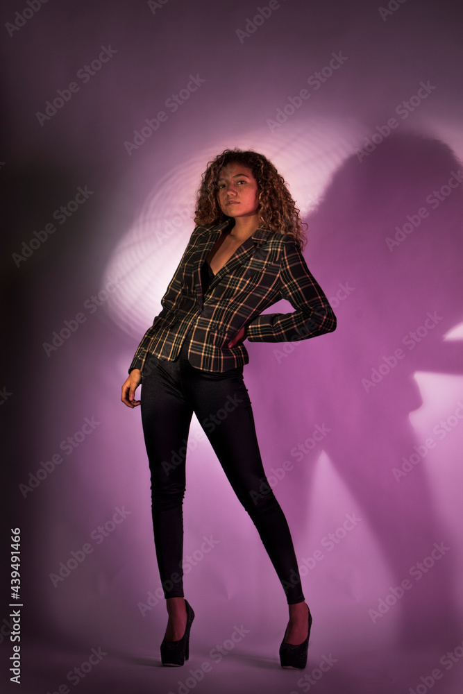 vertical portrait of a curly model wearing a jacket, black pants and high heel shoes in a purple backgroung vertical portrait of a curly model wearing a jacket, black pants and high heel shoes in a purple backgroung