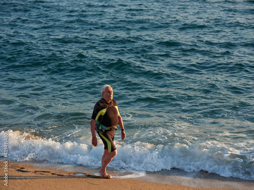 Aged man walking by the shoreline with the watersports suit photo