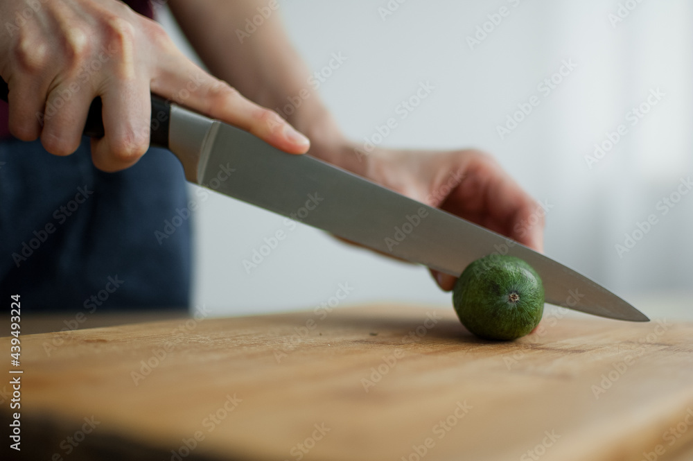 Female hands is cutting a fresh green feijoa fruit on a cut wooden board. Exotic fruits, healthy eating concept Female hands is cutting a fresh green feijoa fruit on a cut wooden board. Exotic fruits, healthy eating concept