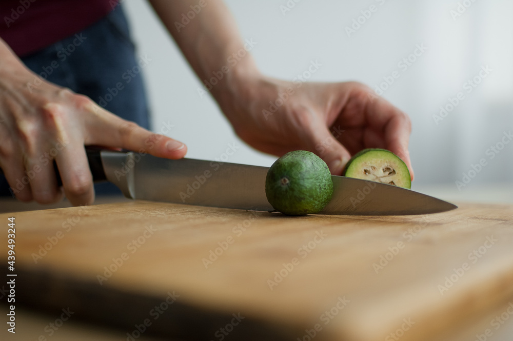 Female hands is cutting a fresh green feijoa fruit on a cut wooden board. Exotic fruits, healthy eating concept Female hands is cutting a fresh green feijoa fruit on a cut wooden board. Exotic fruits, healthy eating concept