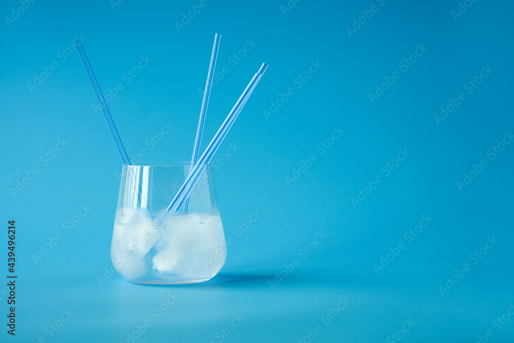 A glass with a clear drink, ice cubes and a few straws on a pale blue background. Copy space. A glass with a clear drink, ice cubes and a few straws on a pale blue background. Copy space.