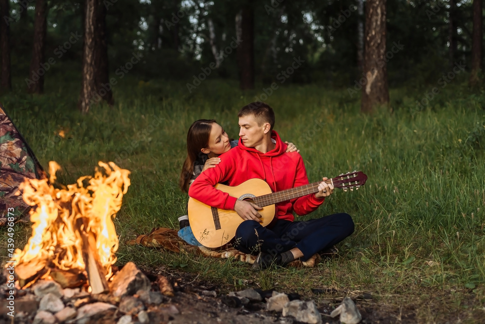 a happy couple in love, a guy and a girl together on a picnic near the campfire with a guitar. romantic weekend picnic a happy couple in love, a guy and a girl together on a picnic near the campfire with a guitar. romantic weekend picnic