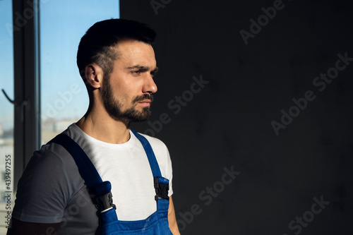 A workman in a blue overalls stands in the shade