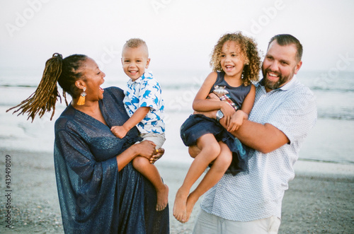 Laughing biracial family on beach at sunset
