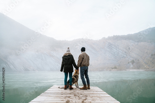 Couple on wooden dock in frozen lake in mountain with dog