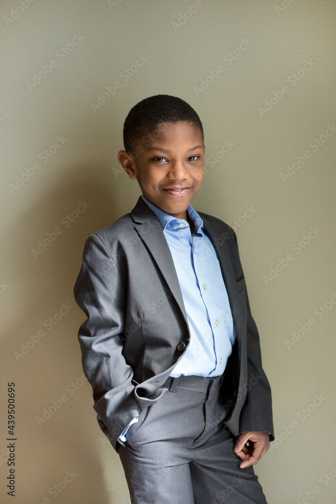 smiling boy in gray suit posing against a wall smiling boy in gray suit posing against a wall