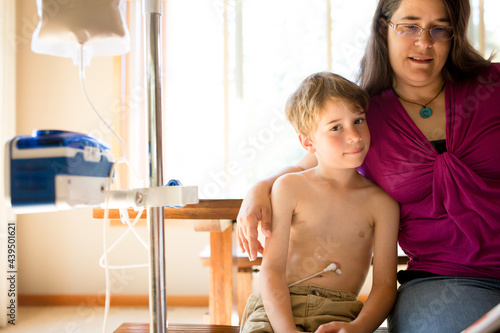 Boy being fed through g-tube smiles at viewer  while mother reads to him 