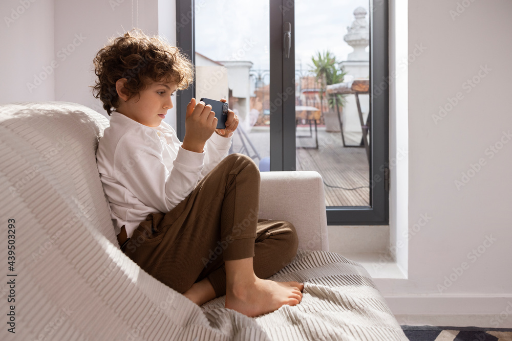 © VICTOR TORRES/Stocksy - Kid using smartphone on sofa