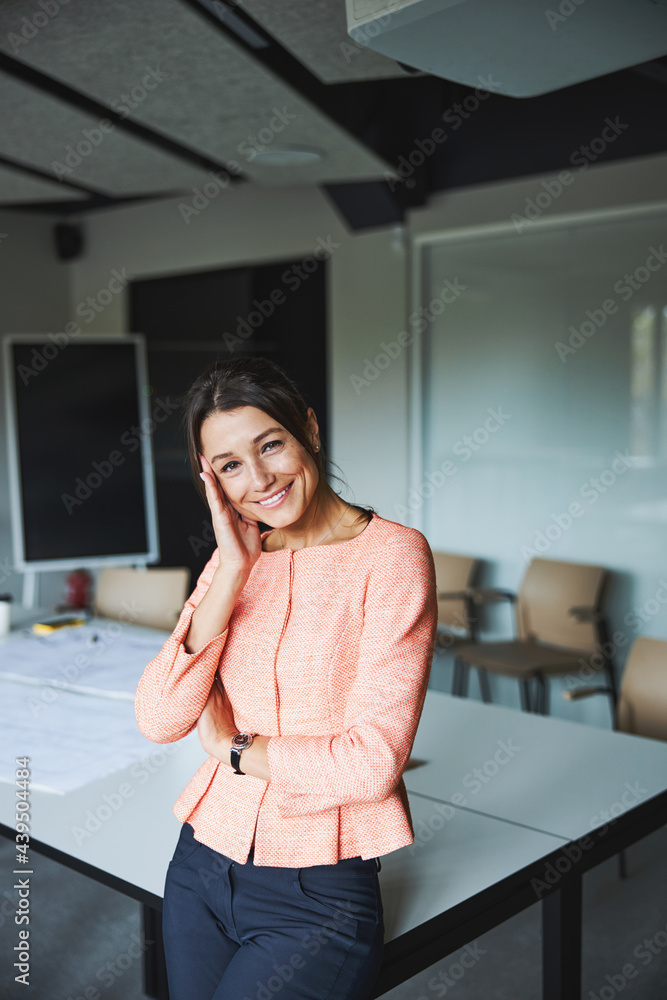 Charming brunette woman business analyst in pink jacket leaning on the work desk in the meeting room Charming brunette woman business analyst in pink jacket leaning on the work desk in the meeting room