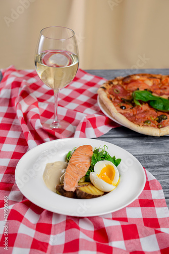 Salmon steak with fresh greenery and boiled eggs served on a white plate with a glass of wine.