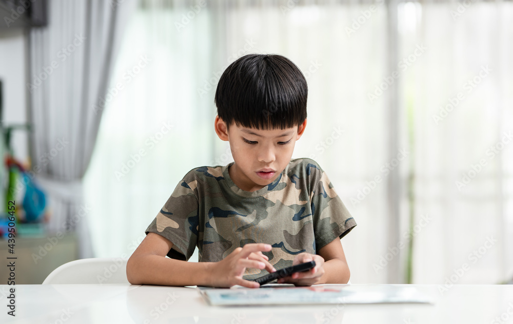 Asian boy with camouflage t-shirt sitting to table browsing smartphone at home. Asian boy with camouflage t-shirt sitting to table browsing smartphone at home.