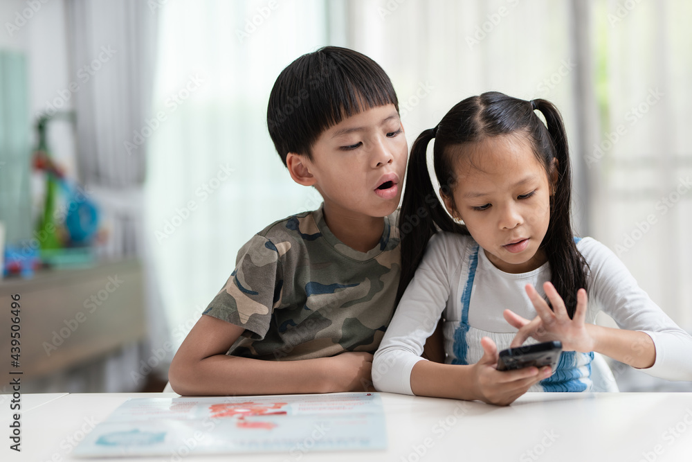 Asian sister playing smartphone. Brother setting next to her and peaking over shoulder. Asian sister playing smartphone. Brother setting next to her and peaking over shoulder.