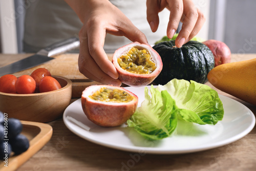 Hands of woman holding sliced passion fruit and preparing vegetables for vegan food cooking on wooden table, Healthy eating