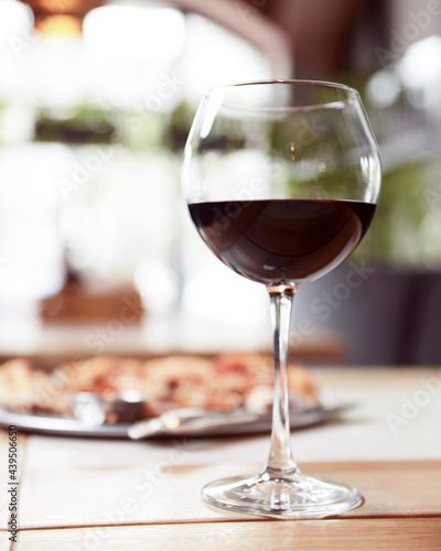 Wine glass filled with red wine on a wooden table with blurred background in restaurant.