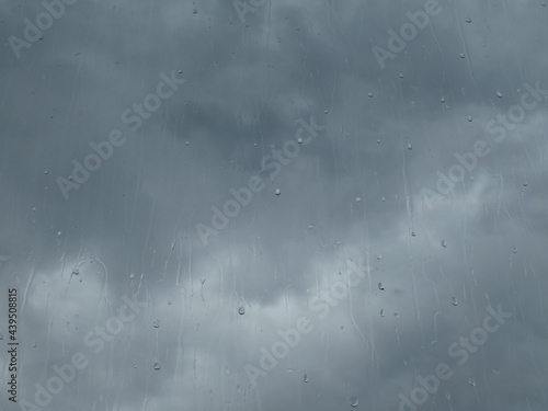 Window glass in a rainy day. Raindrops on window with cloudy sky background
