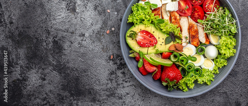 Healthy dinner. Buddha bowl lunch with grilled chicken and avocado, feta cheese, quail eggs, strawberries, nuts and lettuce on gray background. Long banner format. top view