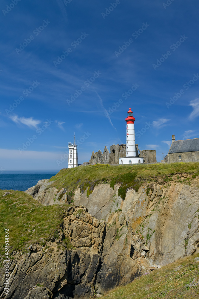 vue sur falaise de granit avec le phare blanc et rouge de la pointe Saint Mathieu et son Abbaye du Finistère en ruine sous un ciel bleu de Bretagne 