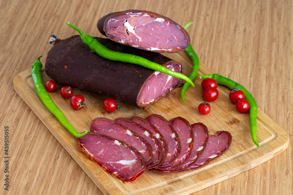 Turkish pastrami on a wooden serving plate. Whole and sliced pastrami